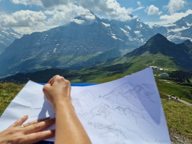 Not all creative work is shared straight away.Sometimes it's sitting on a mountain, pencil in hand, sketching a view that inspires you.This picture was taken while I was sketching the famous Eiger, Mönch, Jungfrau from the Royal Walk at Männlichen during a recent trip to the Swiss Alps. I've been visiting this part of Switzerland for many years and still have sketchbooks from years ago with many of the same views.As with all my ideas some become artworks, others remain sketches and many spend a while quietly developing in the background. My creative pace is often unhurried and reflective; taking time to observe and develop ideas.What's the one place that never gets old, no matter how many times you visit?#GinaBakerArt  #OriginalArt #ContemporaryArt #InspiredByNature #DorsetArtist #HampshireArtist #ChristchurchDorset #SoBo #ArtforYourHome
#JungfrauRegion #SwissAlps