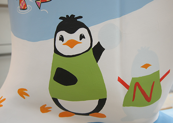 Painted illustration by Gina Baker of a black and white penguin making a snowpenguin. Both are wearing green jumpers and have orange beaks. Letter N. Foorprints in snow. Snowball. Water. Colourful fish
